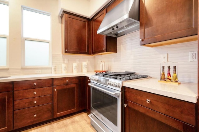 kitchen with stainless steel range, light hardwood / wood-style flooring, decorative backsplash, and wall chimney exhaust hood