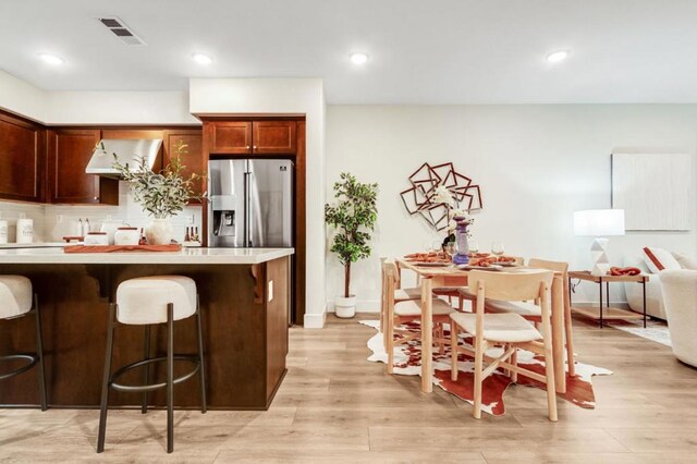 kitchen with a kitchen bar, stainless steel fridge, and light wood-type flooring