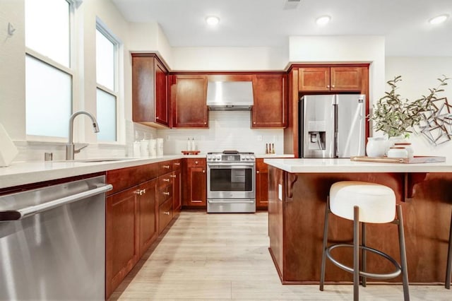 kitchen featuring wall chimney exhaust hood, a kitchen bar, sink, appliances with stainless steel finishes, and decorative backsplash