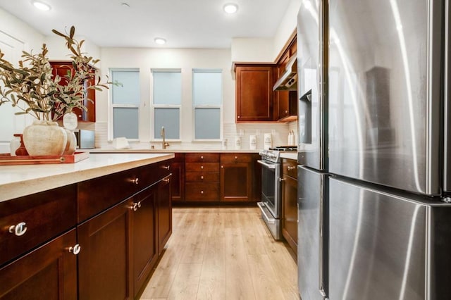 kitchen with sink, stainless steel appliances, light stone counters, decorative backsplash, and light wood-type flooring