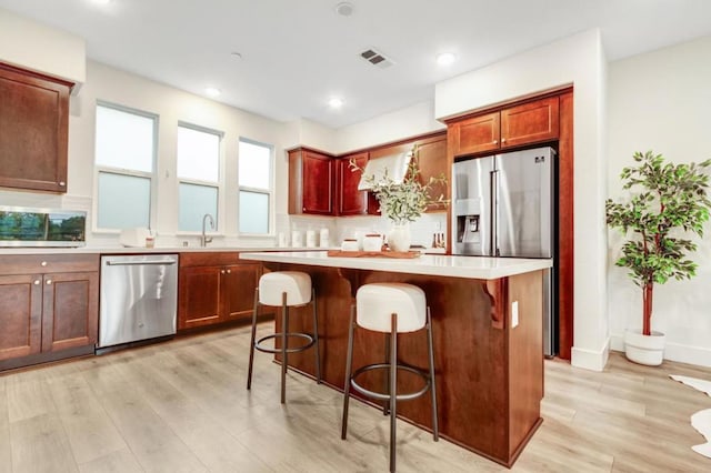 kitchen featuring sink, a kitchen breakfast bar, a center island, light hardwood / wood-style floors, and stainless steel appliances