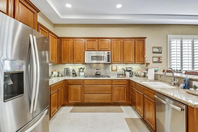 kitchen with stainless steel appliances, light stone countertops, sink, and kitchen peninsula