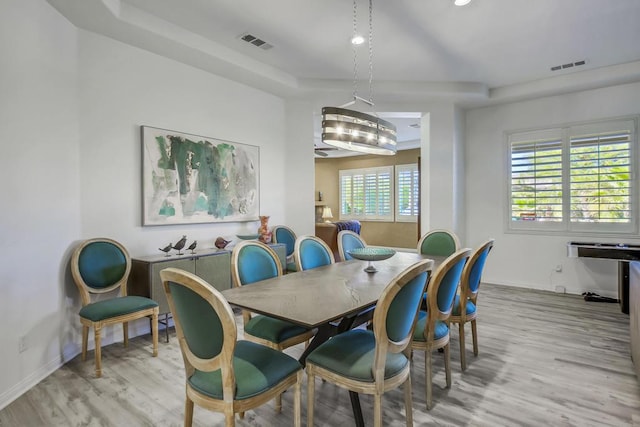 dining room with a tray ceiling and light hardwood / wood-style flooring