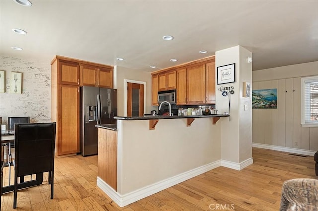 kitchen with appliances with stainless steel finishes, kitchen peninsula, a breakfast bar area, and light wood-type flooring