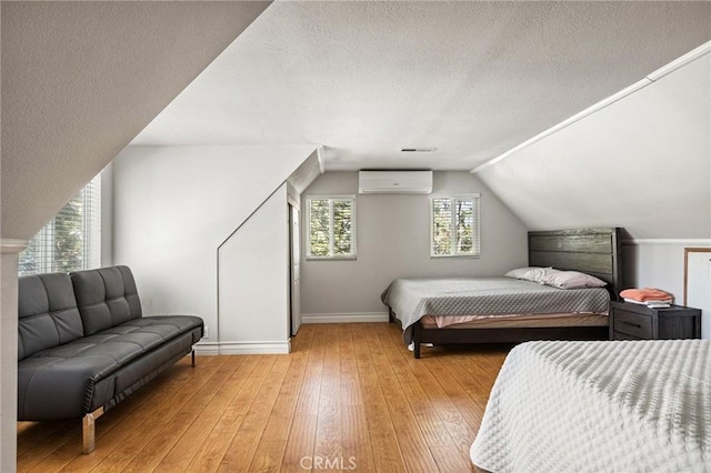 bedroom with an AC wall unit, a textured ceiling, lofted ceiling, and light hardwood / wood-style floors