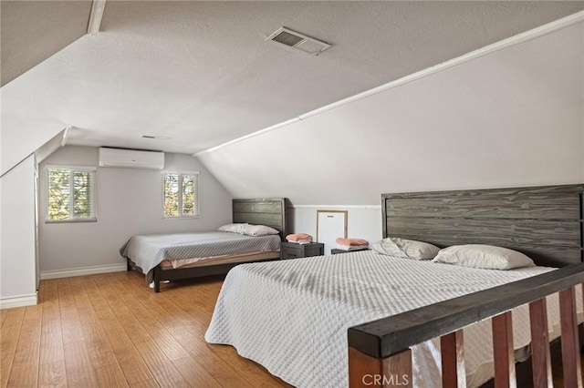 bedroom with hardwood / wood-style flooring, lofted ceiling, a textured ceiling, and a wall unit AC