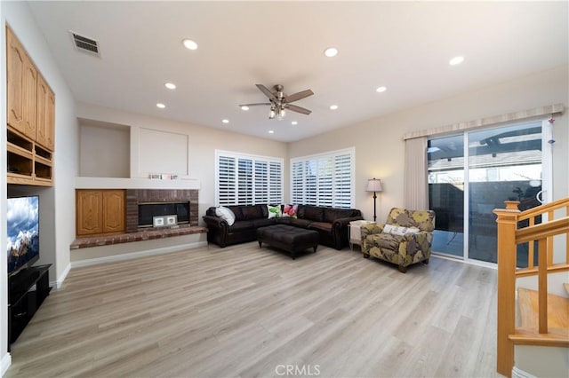 living room with a brick fireplace, light hardwood / wood-style floors, and ceiling fan