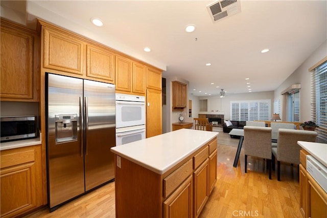 kitchen with ceiling fan, appliances with stainless steel finishes, a center island, and light hardwood / wood-style flooring