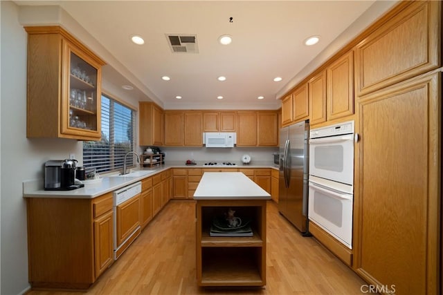 kitchen with sink, white appliances, a center island, and light wood-type flooring