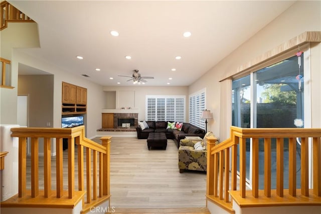 living room featuring ceiling fan, a fireplace, and light hardwood / wood-style floors