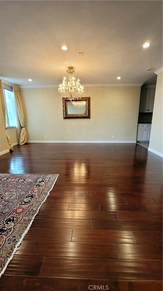 empty room featuring dark wood-type flooring, ornamental molding, and an inviting chandelier