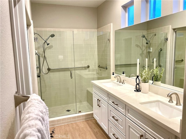 full bathroom with double vanity, a shower stall, a sink, and wood finished floors