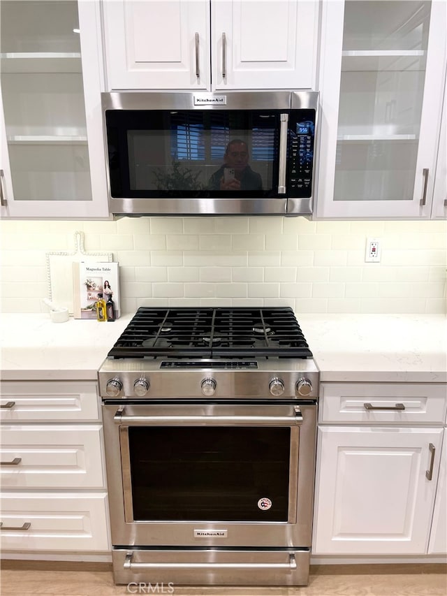 kitchen featuring tasteful backsplash, glass insert cabinets, appliances with stainless steel finishes, light stone counters, and white cabinetry