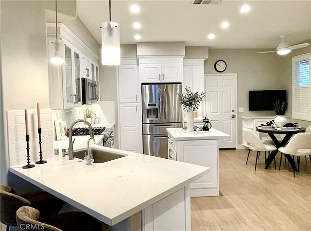 kitchen with stainless steel appliances, a sink, white cabinets, glass insert cabinets, and pendant lighting