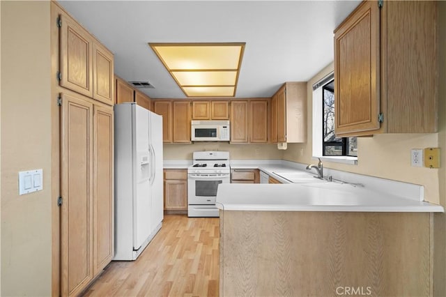 kitchen featuring sink, white appliances, light hardwood / wood-style flooring, and kitchen peninsula