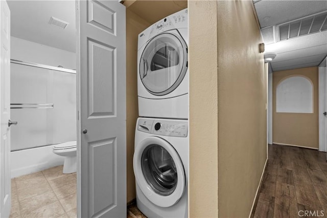 washroom with stacked washer / drying machine and hardwood / wood-style flooring