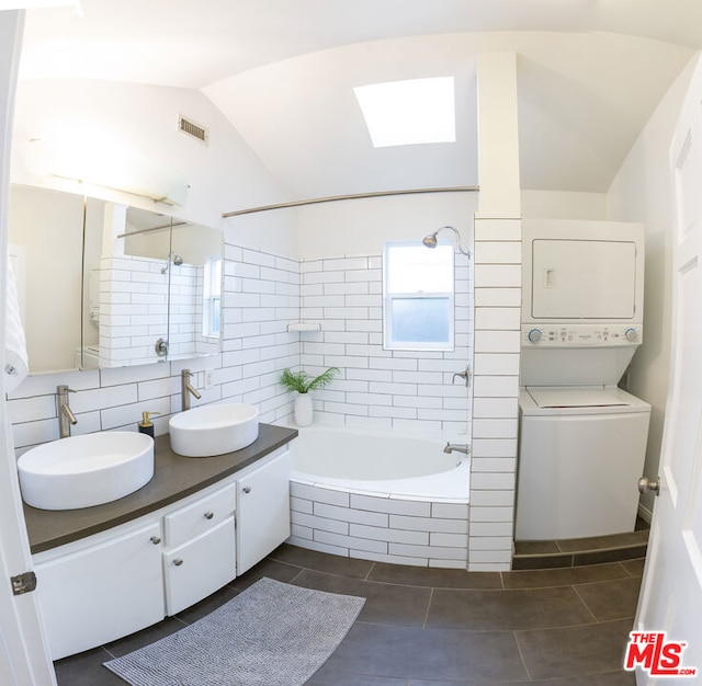 bathroom featuring lofted ceiling, vanity, tiled shower / bath combo, stacked washer / dryer, and backsplash