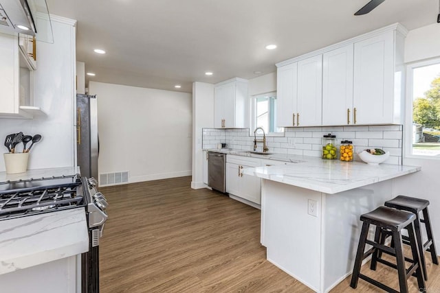 kitchen featuring white cabinetry, appliances with stainless steel finishes, light stone countertops, and a breakfast bar area