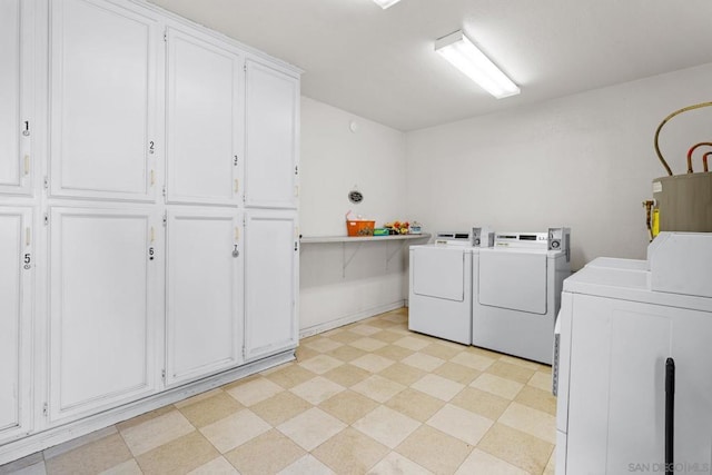 laundry room featuring water heater, washing machine and dryer, and cabinets