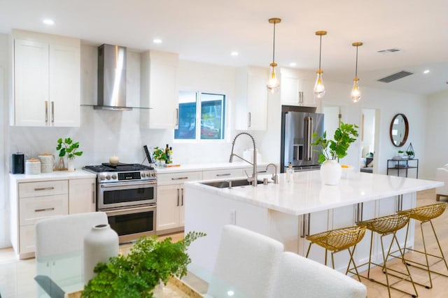 kitchen featuring white cabinetry, stainless steel appliances, an island with sink, and wall chimney exhaust hood