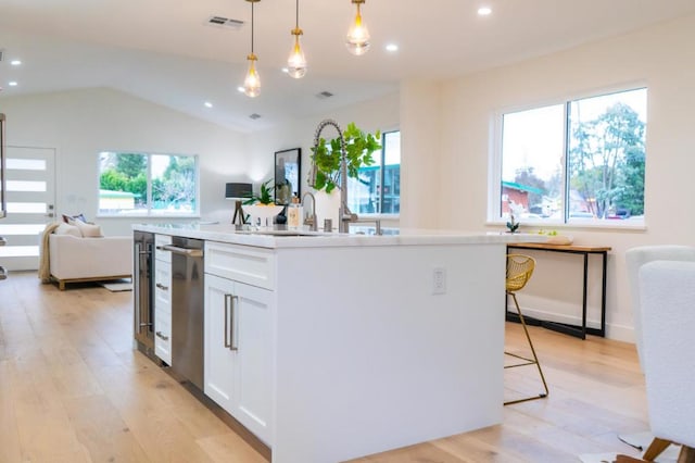 kitchen with white cabinetry, decorative light fixtures, a kitchen island with sink, and light hardwood / wood-style flooring