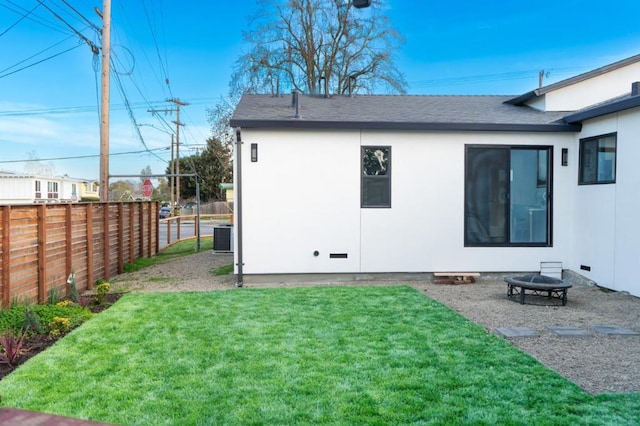 rear view of property featuring cooling unit, a fire pit, and a lawn