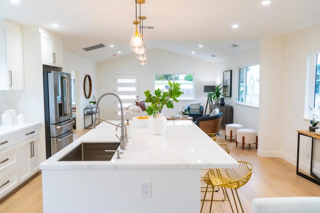 kitchen featuring high end fridge, sink, decorative light fixtures, and a kitchen island with sink