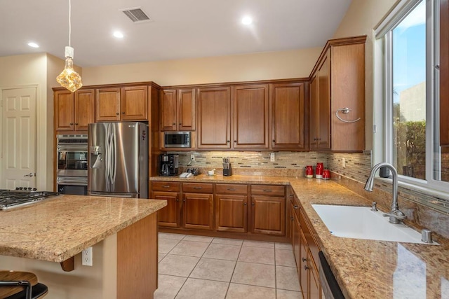 kitchen with sink, appliances with stainless steel finishes, hanging light fixtures, light stone counters, and decorative backsplash