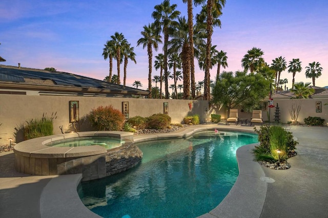 pool at dusk featuring a patio area and an in ground hot tub