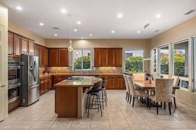 kitchen with stainless steel appliances, a center island, pendant lighting, and light stone counters