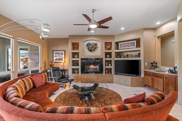 living room featuring light tile patterned flooring, ceiling fan, a tile fireplace, and built in features