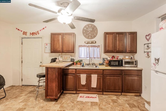 kitchen featuring ceiling fan, a breakfast bar, sink, and white fridge