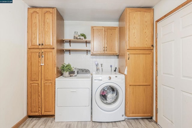 clothes washing area with cabinets, washing machine and dryer, and light hardwood / wood-style flooring