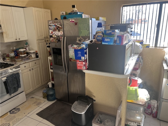 kitchen featuring stainless steel fridge, white gas range, light tile patterned floors, and white cabinets