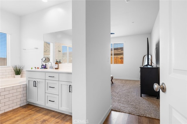 bathroom with hardwood / wood-style flooring, vanity, and tiled tub