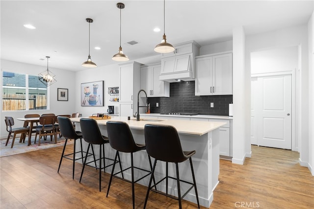 kitchen with light hardwood / wood-style flooring, a kitchen breakfast bar, an island with sink, custom range hood, and pendant lighting