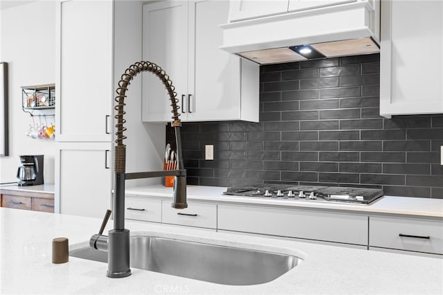 kitchen featuring range hood, tasteful backsplash, white cabinetry, sink, and stainless steel gas cooktop