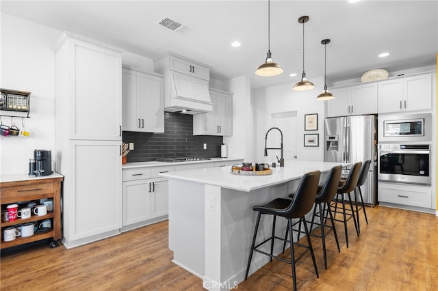 kitchen with stainless steel appliances, hanging light fixtures, a center island with sink, and white cabinets