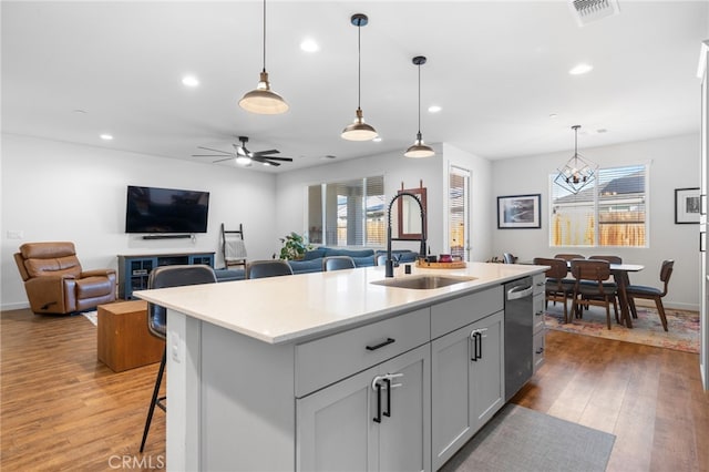 kitchen featuring sink, hardwood / wood-style flooring, a breakfast bar area, a kitchen island with sink, and hanging light fixtures