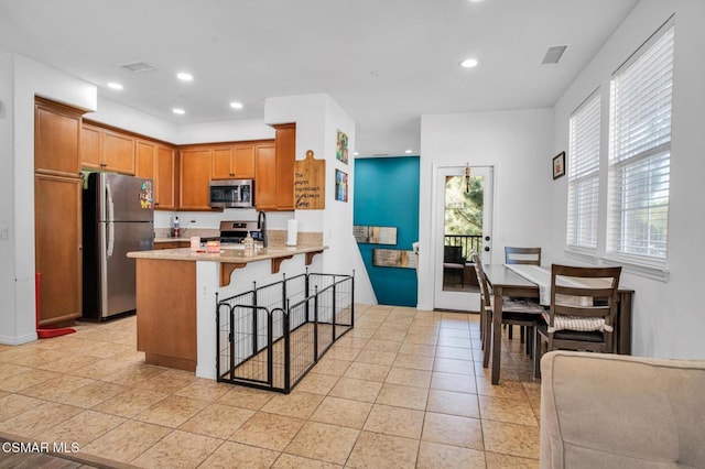 kitchen featuring light tile patterned flooring, appliances with stainless steel finishes, a kitchen breakfast bar, kitchen peninsula, and light stone countertops