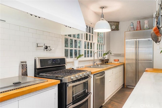 kitchen with sink, wooden counters, appliances with stainless steel finishes, hanging light fixtures, and white cabinets