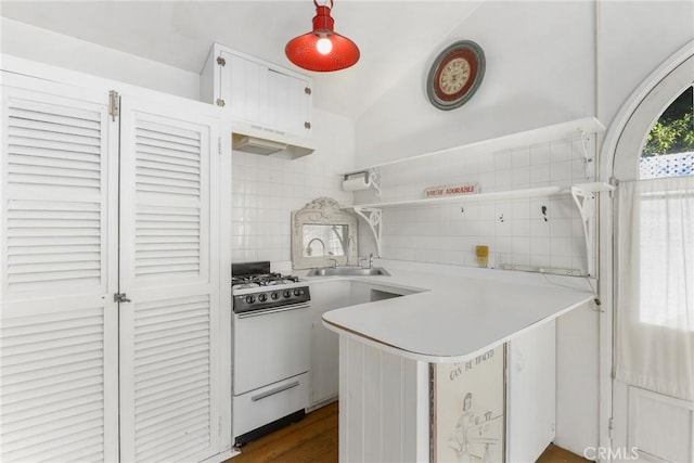 kitchen featuring sink, white range with gas stovetop, kitchen peninsula, white cabinets, and backsplash