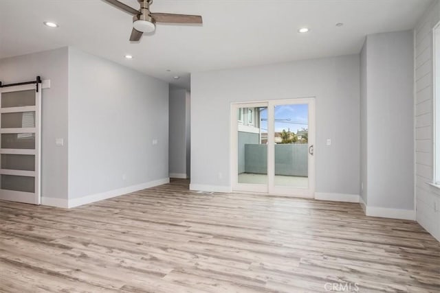 unfurnished room featuring light hardwood / wood-style floors, a barn door, and ceiling fan