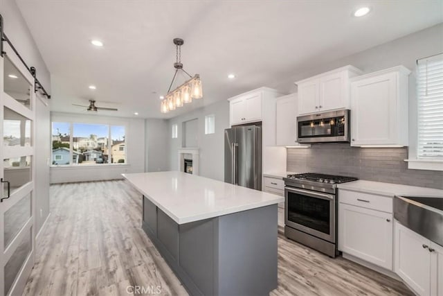 kitchen with pendant lighting, appliances with stainless steel finishes, a kitchen island, and white cabinets