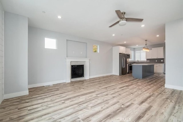 unfurnished living room featuring sink, ceiling fan, and light wood-type flooring