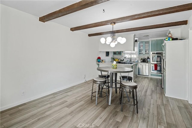 dining area with sink, light hardwood / wood-style floors, a chandelier, and beamed ceiling