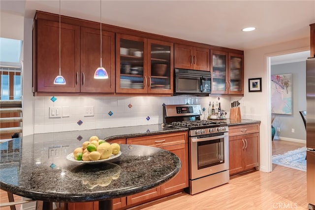 kitchen with hanging light fixtures, stainless steel range with gas cooktop, dark stone countertops, and light hardwood / wood-style flooring