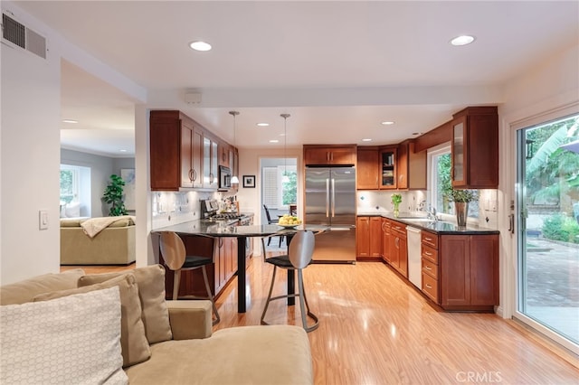 kitchen with sink, light hardwood / wood-style flooring, appliances with stainless steel finishes, decorative light fixtures, and kitchen peninsula