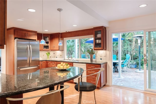 kitchen featuring dishwasher, dark stone countertops, stainless steel fridge, and decorative light fixtures