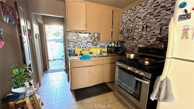 kitchen featuring light tile patterned floors, sink, stainless steel gas range, backsplash, and white refrigerator